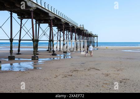 Un uomo e una donna che camminano lungo la spiaggia portando con sé calzature Saltburn by the Sea, Inghilterra, Regno Unito Foto Stock