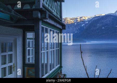 Fotografia di una casa bianca con balcone verde in legno sul lago alpino di Hallstatt al tramonto invernale Foto Stock