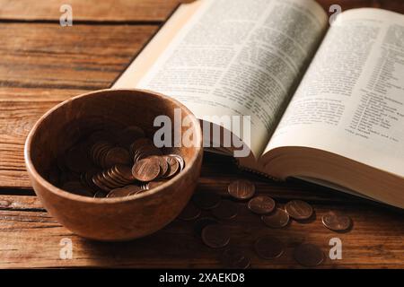 Dona e dai un concetto. Ciotola con monete e Bibbia su un tavolo di legno Foto Stock