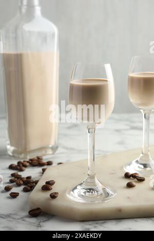 Liquore crema di caffè in bicchieri, fagioli e bottiglia su un tavolo in marmo bianco Foto Stock