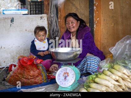 Donna bhutanese con suo figlio che vende verdure in un mercato, Chhoekhor Gewog, Bumthang, Bhutan Foto Stock