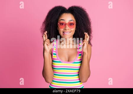 Foto di una canotta in maglieria vestita da donna con un paio di occhiali da sole che morde le labbra con le dita piegate isolate su sfondo rosa Foto Stock