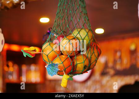 Frutta matura colorata in una borsa in rete verde, sospesa in una stanza illuminata da calore, per creare un'atmosfera accogliente Foto Stock