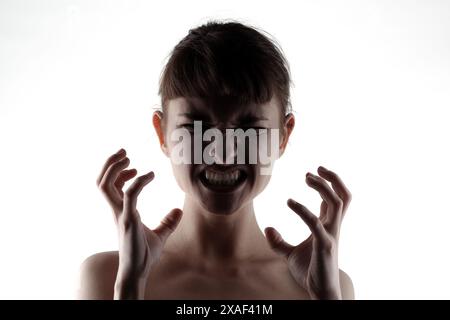 Questa potente immagine cattura una giovane donna in difficoltà, mostrando rabbia e frustrazione intensa con l'espressione facciale e i gesti delle mani Foto Stock