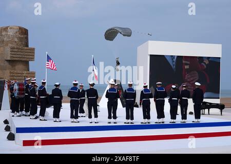 Normandia, Francia. 6 giugno 2024. Un paracadutista (C) arriva come una banda di musicisti della Marina francese suona durante la cerimonia commemorativa internazionale a Omaha Beach in occasione del 80° anniversario dello sbarco alleato del D-Day della seconda guerra mondiale in Normandia, a Saint-Laurent-sur-Mer, nella Francia nord-occidentale, il 6 giugno 2024Fotografia dell'Ambasciata degli Stati Uniti France/UPI. Crediti: UPI/Alamy Live News Foto Stock