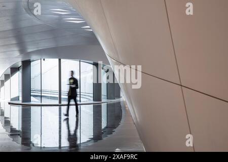 Qualcuno che cammina attraverso lo spazio tra gli uffici e la reception principale. BEEAH Headquarters, Sharjah, Emirati Arabi Uniti. Architetto: Zaha Foto Stock
