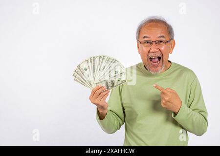 Ritratto asiatico sorridente vecchio sta tenendo un mucchio di banconote e sta puntando lo studio shot Foto Stock