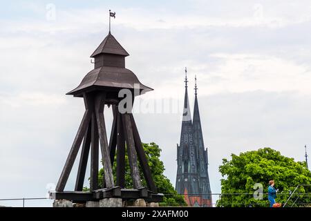 La torre campanaria in legno del 1756 si erge sui resti di un muro del castello che andò distrutto in un incendio nel 1702, con le guglie della cattedrale di Uppsala che si stagliano dietro. Vista dalla piazza del castello più alta, un passante che passa a destra. Drottning Christinas väg, Uppsala, Contea di Uppsala, Svezia. Foto Stock