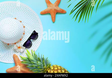 Concetto di design dello sfondo estivo. Vista dall'alto con stelle marine, ananas, cappello, occhiali da sole e foglie di palma su sfondo blu. Foto Stock