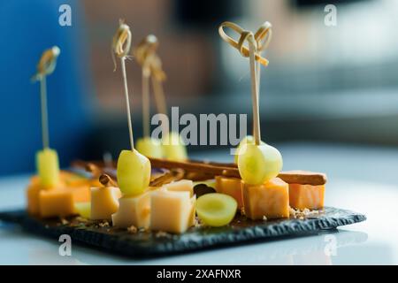 Affettare diversi tipi di formaggio e di uva. Antipasto con formaggio e uva su un bordo nero su sfondo bianco Foto Stock