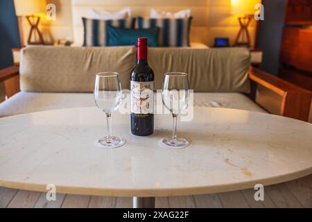 Vista ravvicinata di una bottiglia di vino rosso di benvenuto con due bicchieri su un tavolo di marmo in una lussuosa camera del resort Secrets the Vine. Cancún. Messico. Foto Stock