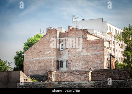 Questa immagine cattura una facciata danneggiata di un edificio residenziale nel cuore di Belgrado, in Serbia. Le pareti in mattoni intemprati sono in netto contrasto con Foto Stock