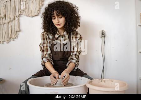 La giovane donna ceramista si è concentrata sulla creazione di piatti in ceramica utilizzando la ruota di un vasaio in un accogliente ambiente da studio. Foto Stock