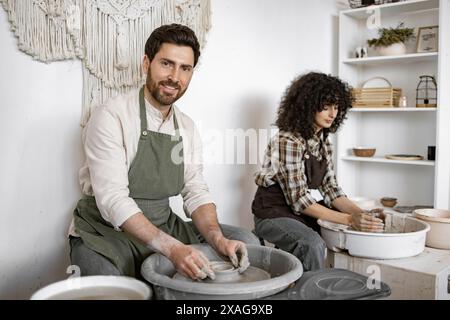 Uomo e donna che creano ceramiche su ruote di ceramica. Sono concentrati e immersi nella loro arte, lavorando insieme in un ambiente creativo. Foto Stock