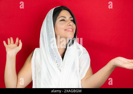 Ritratto di una donna con una sciarpa bianca in studio. giovane donna mediorientale con sfondo rosso Foto Stock
