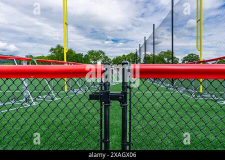 Recinzione nera a maglie a catena, cancello, con cappellino rosso e campo da softball/baseball sullo sfondo. Foto Stock