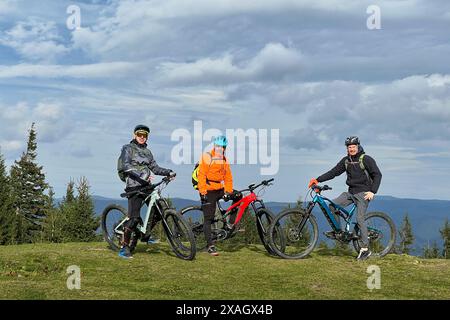 Gruppo di ciclisti uomini che cavalcano biciclette elettriche all'aperto. Ritratto di turisti felici che riposano sulla cima della collina, godendo di uno splendido paesaggio montano. Concetto di sport, svago attivo e natura. Foto Stock