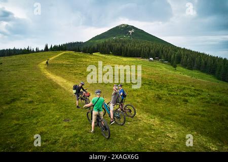 Gruppo di ciclisti uomini che cavalcano biciclette elettriche all'aperto. Turisti felici che riposano sulla cima della collina, godendo di uno splendido paesaggio montano. Concetto di sport, svago attivo e natura. Foto Stock