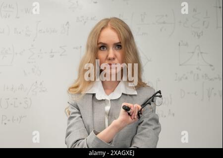 Una donna caucasica si trova ad una lavagna con formule scritte. Foto Stock