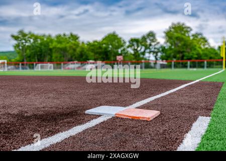 Vista del campo di softball sintetico del manto erboso della scuola superiore, prima base con seconda base di sicurezza arancione, guardando verso la piastra di base. Foto Stock