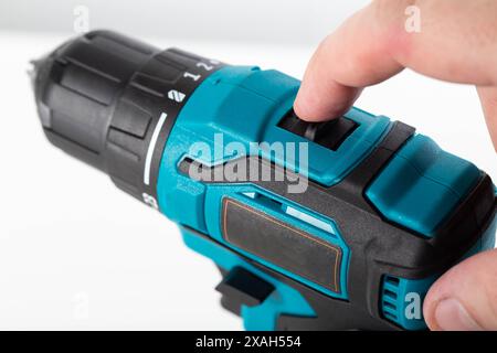 Il dito di un lavoratore commuta l'interruttore del senso di rotazione su un trapano avvitatore, primo piano, settore industriale Foto Stock