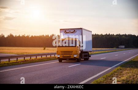 Un furgone commerciale refrigerato a basso tonnellaggio trasporta prodotti deperibili in estate su una strada di campagna sullo sfondo del tramonto. Industria Foto Stock