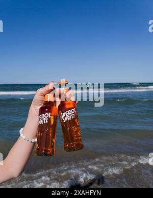 Rimini, Italia, 7 giugno 2024 - mano con due bottiglie Aperol Spritz pronta da bere sullo sfondo del mare Foto Stock