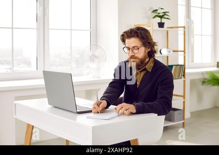 Uomo d'affari che scrive su un notebook mentre è seduto alla scrivania con un computer portatile Foto Stock