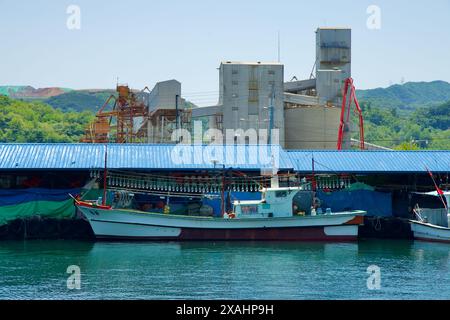 Samcheok City, Corea del Sud - 18 maggio 2024: Una barca da pesca ormeggiata di fronte agli edifici industriali del porto di Samcheok, evidenziando l'intersezione tra t Foto Stock