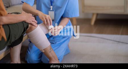 Primo piano di un assistente asiatico che bendava la gamba di una donna anziana a casa. Concetto di assistenza agli anziani e gestione delle ferite Foto Stock