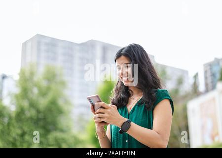 Sorridente giovane donna che usa il suo smartphone in città Foto Stock