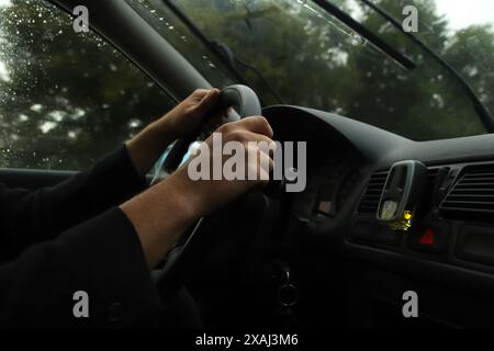 Tenere premuto il volante durante la guida sotto la pioggia. Viaggia su strada a tutta velocità in una giornata di pioggia. Mani di una persona che tiene il volante in posizione pesante Foto Stock