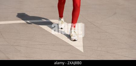 primo piano di una donna runner con una freccia dipinta sulla strada Foto Stock