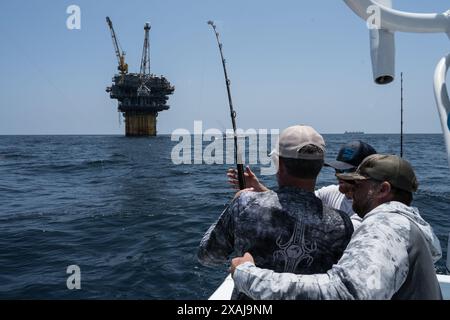 Un pescatore si avvolge in un tonno pescato vicino a piattaforme petrolifere galleggianti nel Golfo del Messico, illustrando la giustapposizione di pesca ricreativa e petrolio offshore Foto Stock