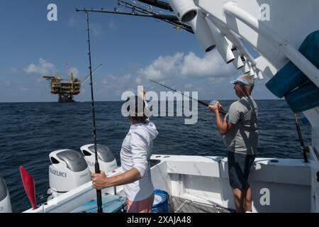 Un pescatore si avvolge in un tonno pescato vicino a piattaforme petrolifere galleggianti nel Golfo del Messico, illustrando la giustapposizione di pesca ricreativa e petrolio offshore Foto Stock