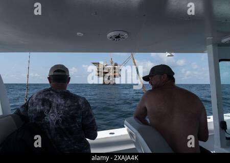 Un pescatore si avvolge in un tonno pescato vicino a piattaforme petrolifere galleggianti nel Golfo del Messico, illustrando la giustapposizione di pesca ricreativa e petrolio offshore Foto Stock