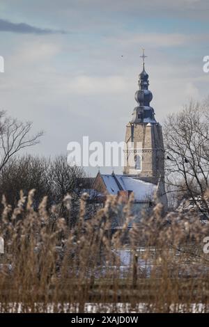 Vista invernale verso Mespelare e la chiesa di Sant'Aldegonde, vicino a Dendermonde in Belgio. Guardando attraverso il fiume Dender attraverso il bellissimo lato illuminato gr Foto Stock