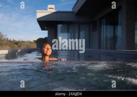 Una donna si crogiola al sole nella tranquilla piscina a sfioro. Foto Stock