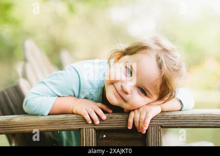 La bambina sorride con gli occhi blu seduto nel cortile Foto Stock