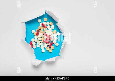 Lacerazione nella carta bianca che rivela pillole e capsule sotto su sfondo blu. Concetto di farmaco, spazio per il testo. Foto Stock
