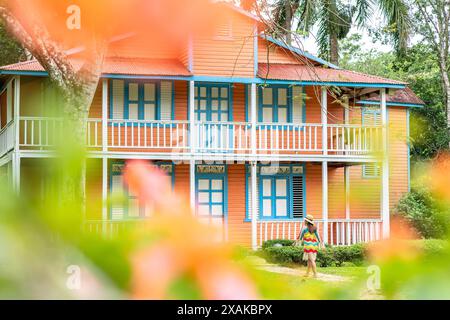 Nord America, Caraibi, isola di Hispaniola, Repubblica Dominicana, Monte Plata, Bayaguana, campo Aventura, donna in abito colorato cammina verso una pittoresca casa in legno Foto Stock