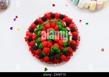 Vista dall'alto di gustosi dolci in gelatina a forma di fragole rosse e di more nere e rosse su un piatto su sfondo bianco. Foto Stock