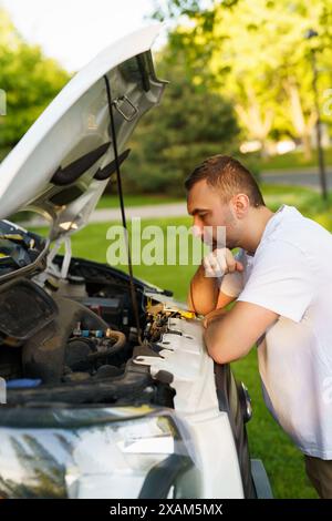 L'uomo stressato ha problemi con la sua auto rotta e guarda con frustrazione il motore guasto Foto Stock