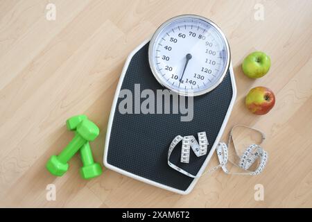 Concetto di fitness, dieta e perdita di peso, bilancia personale con metro a nastro, manubri verdi e due mele su un pavimento in legno, vista ad angolo alto da abov Foto Stock