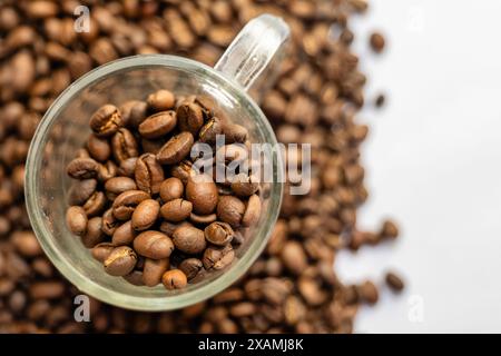 Una tazza da caffè trasparente cosparge di chicchi appena tostati, evocando l'aroma di un caffè perfetto. Foto Stock