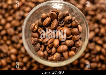 Una tazza di caffè in vetro cosparge di chicchi di caffè appena tostati, creando una scena invitante per gli amanti del caffè Foto Stock