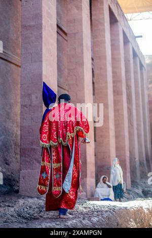 Ortodox uomo sacerdote in tessuto rosso che cammina alle pareti della chiesa monolitica ortodox di Bete Medham Alem, Lalibela, regione di Amhara, Etiopia. Foto Stock