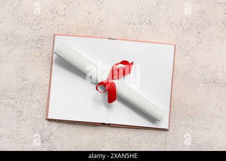 Diploma con nastro rosso e libro aperto su sfondo grunge bianco Foto Stock