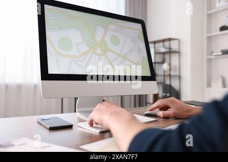 Cartografo che lavora con una mappa catastale al computer al tavolo di legno in ufficio, primo piano Foto Stock