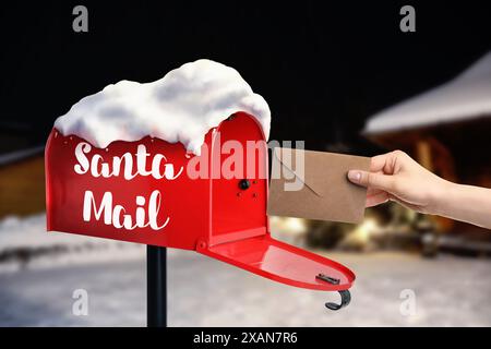 Donna che mette la lettera a Babbo Natale nella cassetta della posta all'aperto, primo piano. Tradizione natalizia Foto Stock